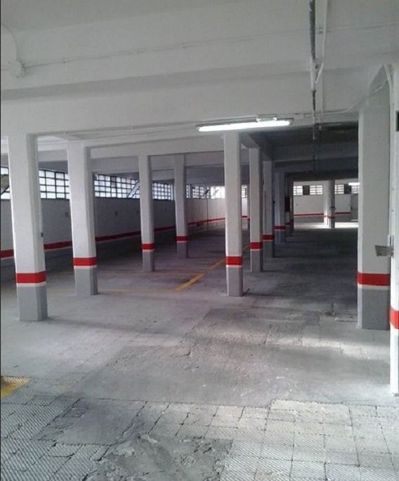 Garaje vacío con pilares blancos marcados con franjas rojas y grises y suelo de hormigón.