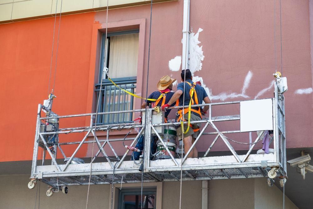 Obreros en un andamio suspendido repintando la pared exterior de un edificio.